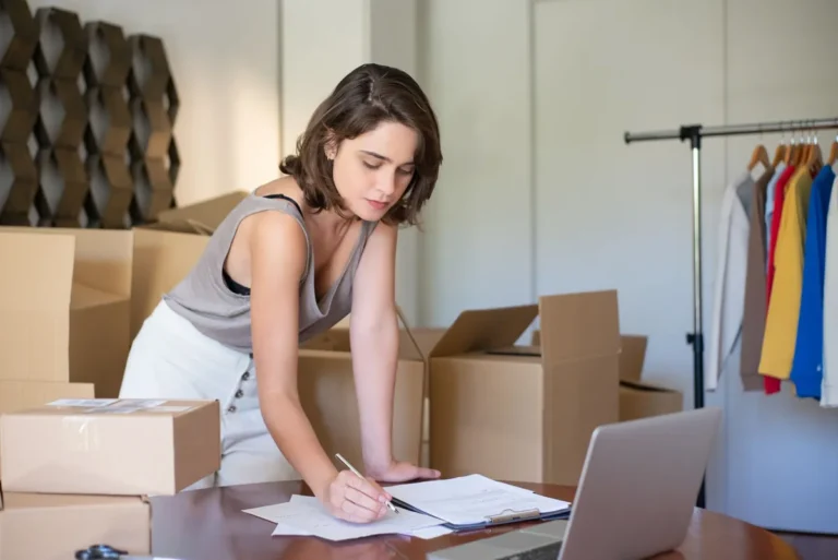 Starter die thuis aan een bureau met laptop bestellingen inpakt voor haar nieuwe webshop